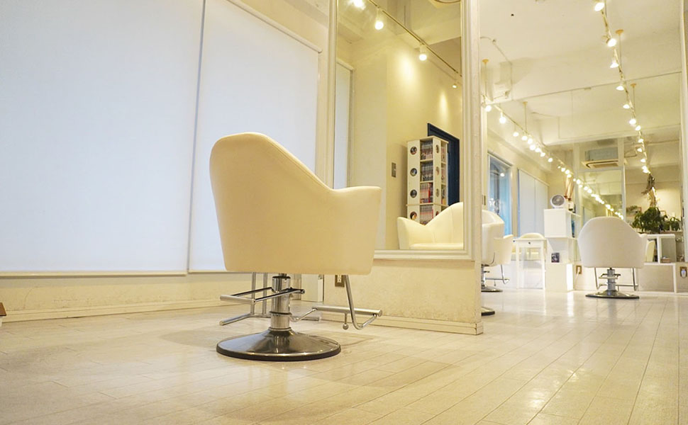 大きな鏡と施術用の椅子が写った白を基調とした明るい店内写真