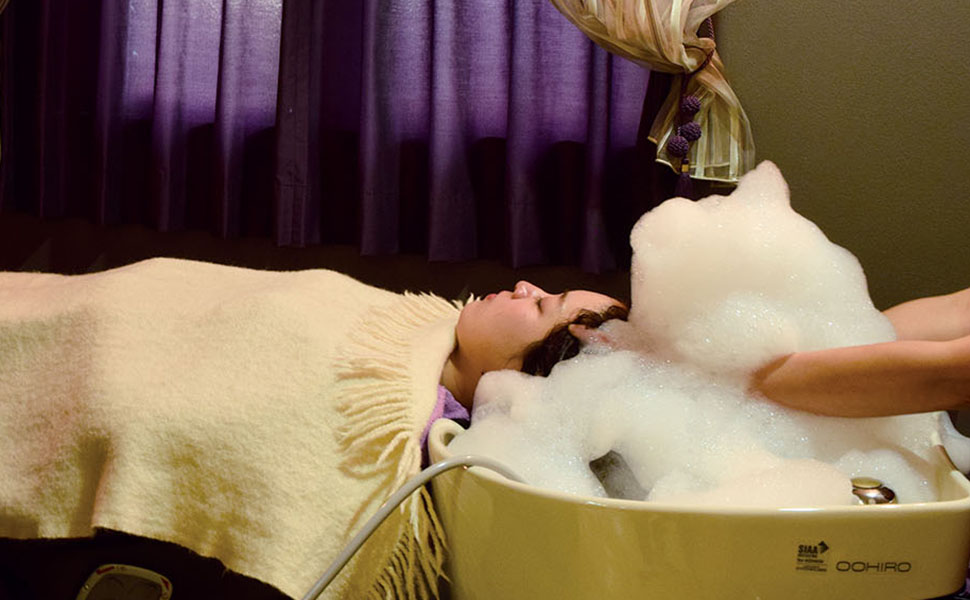 たっぷりの泡で髪を洗いながらヘッドスパを受けるシャンプー台に寝る女性