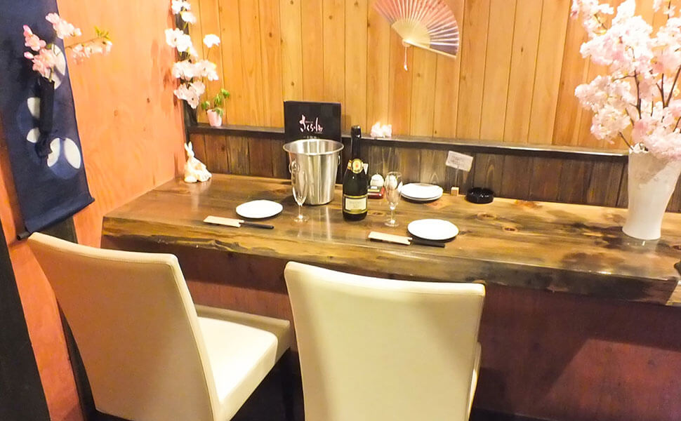 シャンパンボトルとグラス、お皿、箸がテーブルの上に並ぶ、横並びの椅子のカップルシートの席。