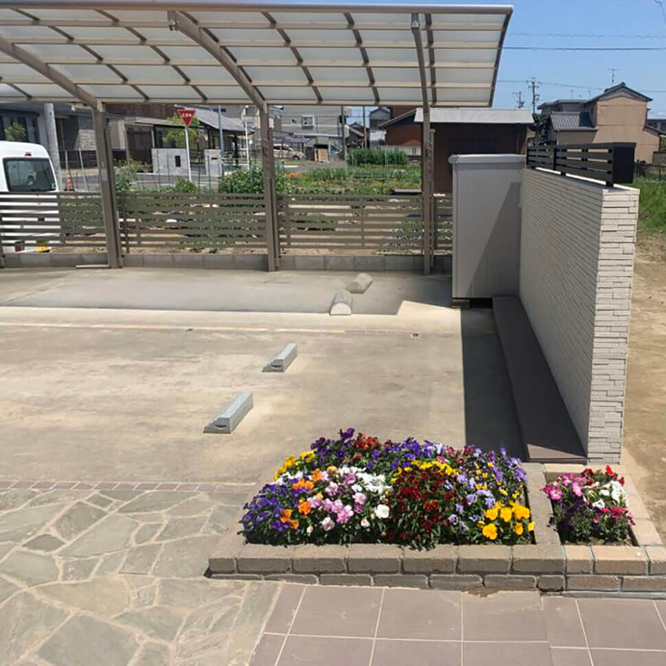 岐阜県柳津町にあるBL gardenの玄関アプローチ1例。駐車場後ろには1㎡程度の花壇が施工され、パンジーなどのカラフルな花が咲いている。