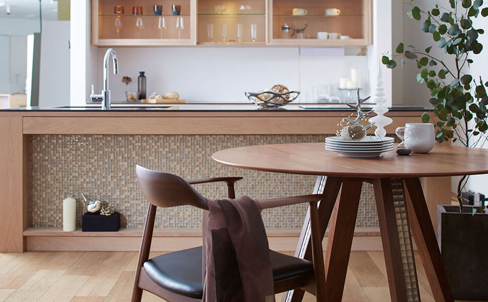 ダークブラウンな円形のテーブルと椅子。その奥にはガラスタイルで造作されたキッチン。