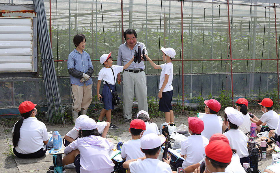 伊藤さんと小学生がなすの大きさ比べをしている様子